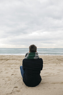 Rückenansicht eines Mannes, der im Winter am Strand sitzt und in die Ferne schaut - JRFF01509