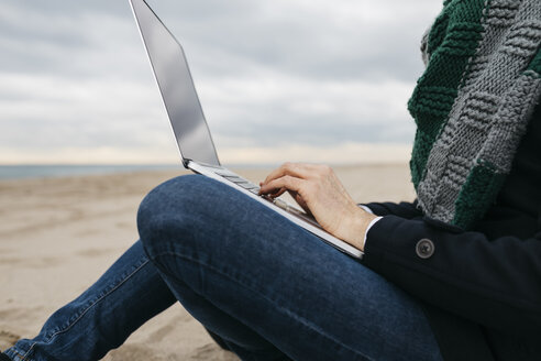 Geschäftsmann, der im Winter am Strand sitzt und einen Laptop benutzt, Teilansicht - JRFF01510