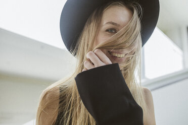 Portrait of laughing blond woman wearing black hat - KMKF00139
