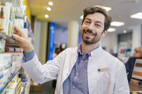 Porträt einer lächelnden Apothekerin mit Medikamenten im Regal in einer Apotheke, lizenzfreies Stockfoto