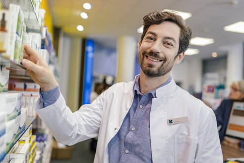 Porträt einer lächelnden Apothekerin mit Medikamenten im Regal in einer Apotheke - MFF04284