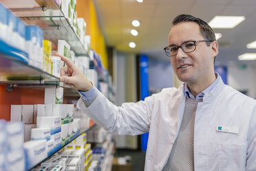 Portrait of smiling pharmacist with medicine at shelf in pharmacy - MFF04285