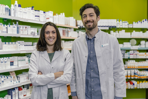 Porträt von zwei lächelnden Apothekerinnen am Regal mit Medikamenten in der Apotheke, lizenzfreies Stockfoto