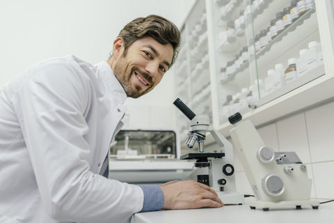 Porträt eines lächelnden Mannes, der ein Mikroskop im Labor benutzt, lizenzfreies Stockfoto