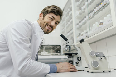 Porträt eines lächelnden Mannes, der ein Mikroskop im Labor benutzt - MFF04307