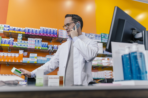 Apothekerin telefoniert am Tresen in der Apotheke, lizenzfreies Stockfoto