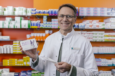 Portrait of smiling pharmacist holding tablet package and prescription in pharmacy - MFF04334