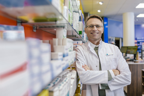 Portrait of smiling pharmacist leaning against shelf with medicine in pharmacy stock photo