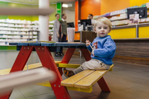 Little boy sitting on bench in pharmacy with parents in background stock photo