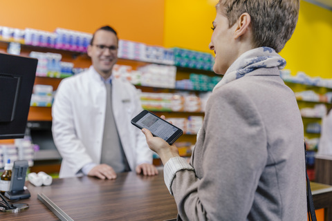Smiling woman with cell phone at counter in pharmacy stock photo