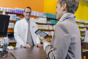 Lächelnde Frau mit Handy am Tresen einer Apotheke - MFF04344