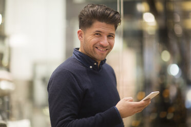 Portrait of laughing man with cell phone in a shopping mall - SGF02138