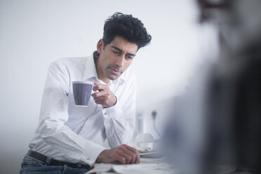 Porträt eines Geschäftsmannes, der morgens zu Hause Kaffee trinkt und Zeitung liest - SGF02139