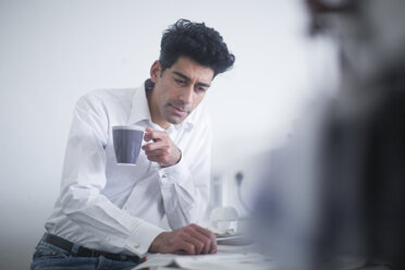 Portrait of businessman drinking coffee while reading newspaper in the morning at home - SGF02139