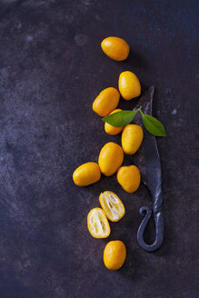 Geschnittene und ganze Kumquats, Blätter und altes Messer auf rostigem Boden - CSF28697