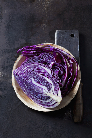 Geschnittener Rotkohl in einer Schüssel und ein Hackbeil auf dunklem Grund, lizenzfreies Stockfoto