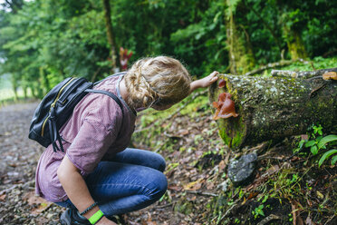 Costa Rica, Frau betrachtet einen Pilz auf einem Baumstamm - KIJF01848