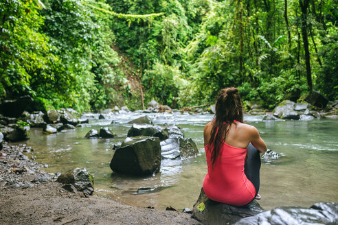 Costa Rica, Arenal Volcano National Park, Frau sitzt auf einem Stein des Flusses Fortuna - KIJF01855