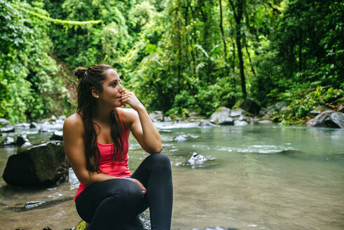 Costa Rica, Arenal Volcano National Park, Frau sitzt auf einem Stein des Flusses Fortuna - KIJF01856