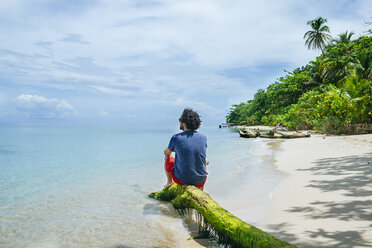 Panama, Bocas del Toro, Cayo Zapatilla, Mann sitzt auf Baumstamm am Strand - KIJF01869