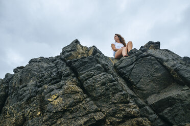 Costa Rica, Woman sitting on rocks, view from below - KIJF01884