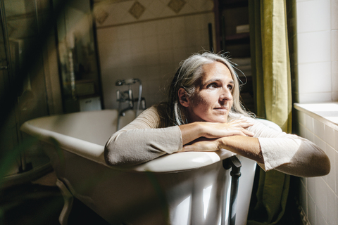 Porträt einer traurigen Frau, die angezogen in der Badewanne sitzt, lizenzfreies Stockfoto