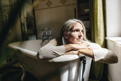 Porträt einer traurigen Frau, die angezogen in der Badewanne sitzt - KNSF03459