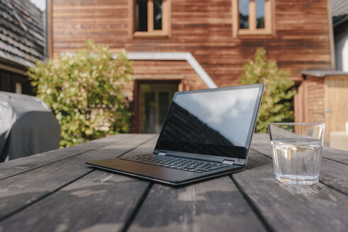 Laptop und Glas Wasser auf dem Tisch auf der Terrasse - KNSF03475