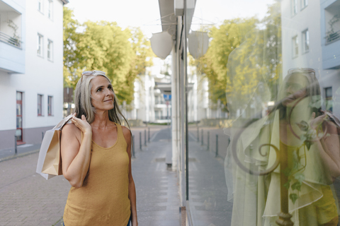 Porträt einer lächelnden Frau mit Einkaufstüten, die in ein Schaufenster schaut, lizenzfreies Stockfoto