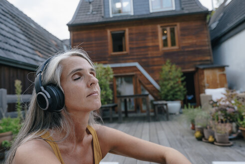 Porträt einer reifen Frau, die auf einer Terrasse mit Kopfhörern Musik hört - KNSF03495