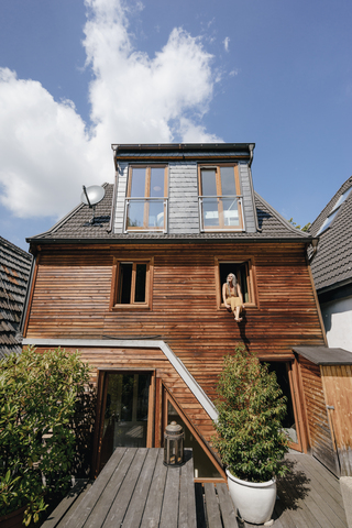 Frau sitzt auf der Fensterbank ihres Hauses und nimmt ein Sonnenbad, lizenzfreies Stockfoto