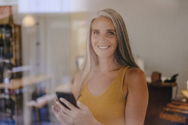 Porträt einer lächelnden Geschäftsfrau mit Mobiltelefon in ihrem Geschäft - KNSF03521
