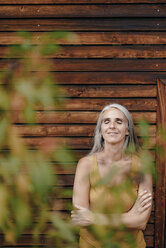 Porträt einer lächelnden reifen Frau, die vor einer Holzfassade steht - KNSF03524