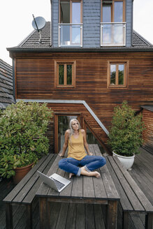 Woman relaxing on garden table at the backyard of her house - KNSF03531