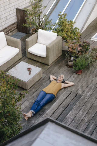 Frau entspannt sich auf Terrasse und hört Musik mit Kopfhörern, lizenzfreies Stockfoto