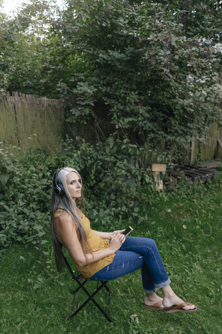 Woman with cell phone sitting in the garden listening music with headphones stock photo