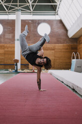 Junger Mann macht akrobatische Übungen im Fitnessstudio - OCAF00015