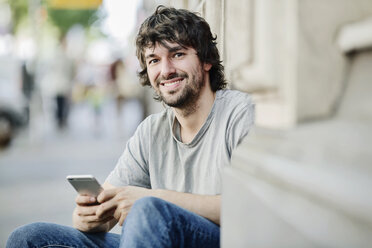 Porträt eines lächelnden jungen Mannes mit Mobiltelefon im Freien - JATF00978