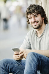 Porträt eines lächelnden jungen Mannes mit Mobiltelefon im Freien - JATF00979