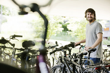 Porträt eines lächelnden jungen Mannes, der sein Fahrrad parkt - JATF00984