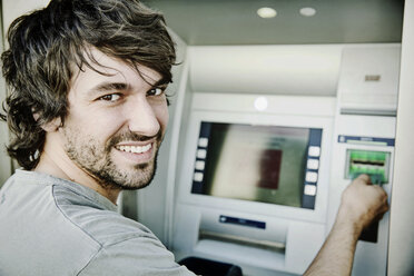 Porträt eines lachenden jungen Mannes an einem Geldautomaten - JATF00986