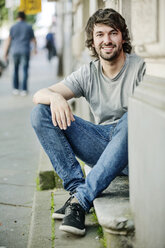 Portrait of smiling young man sitting on step outdoors - JATF00987