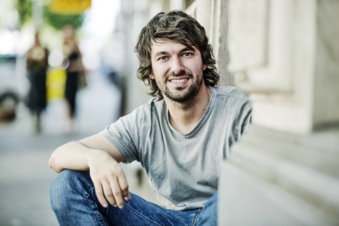 Porträt eines lächelnden jungen Mannes, der im Freien sitzt, lizenzfreies Stockfoto