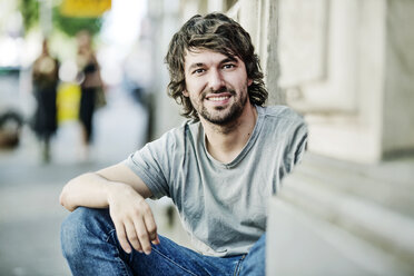Porträt eines lächelnden jungen Mannes, der im Freien sitzt - JATF00988