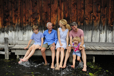 Family sitting together on jetty splashing with water - ECPF00164