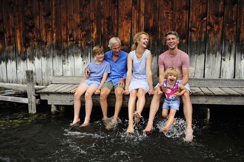 Familie sitzt zusammen auf dem Steg und spritzt mit Wasser, lizenzfreies Stockfoto