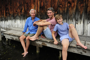 Boy sitting with grandfather and father together on jetty in summer - ECPF00168