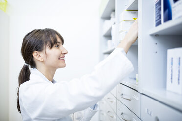 Smiling pharmacist checking medicine at cabinet in pharmacy - WESTF23912