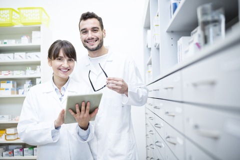 Porträt von zwei lächelnden Apothekerinnen mit Tablet in der Apotheke, lizenzfreies Stockfoto