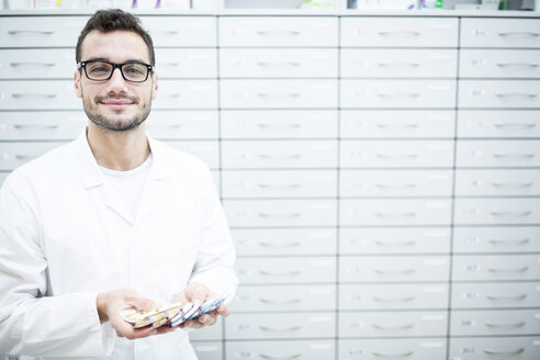 Porträt einer lächelnden Apothekerin, die Tablettenpackungen an einem Schrank in einer Apotheke hält - WESTF23932